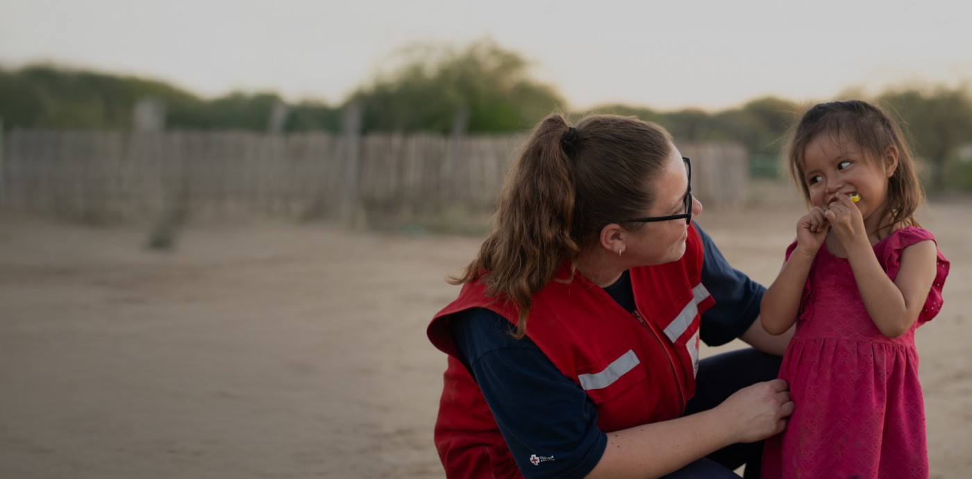 Una mujer del equipo de Cruz Roja junto a una niña comiendo un pan